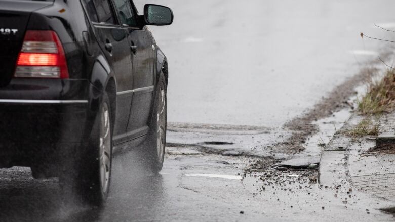 A car is pictured running on a wet road, with a power pole on the pavement.