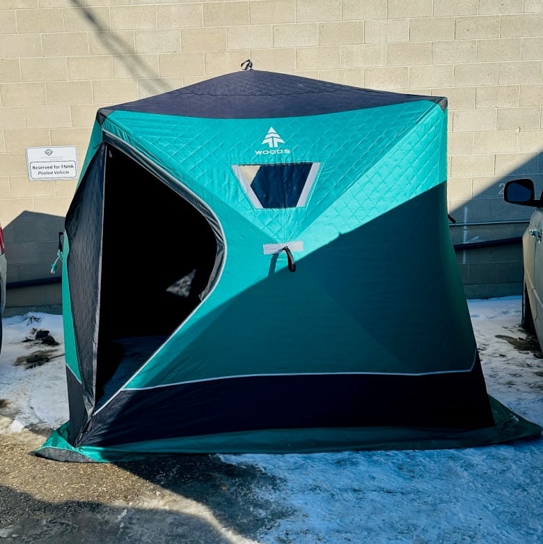 A blue and black ice fishing tent set up in a parking spot between two cars. 