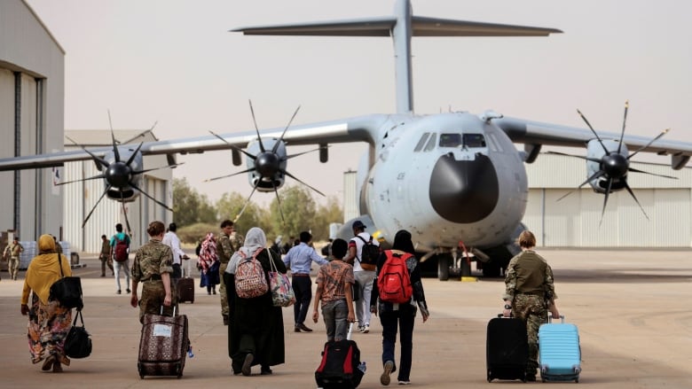 People rolling luggage walk toward a plane on the tarmac.