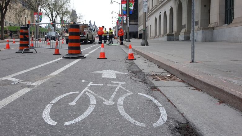 Workers in orange and yellow use a tank and hose to paint a bike lane.