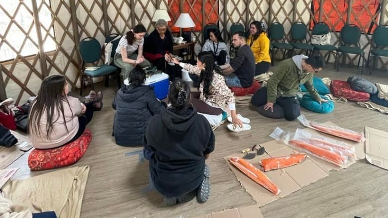 An Inuk elder shares Arctic char with a group of Indigenous youth inside a yurt. 