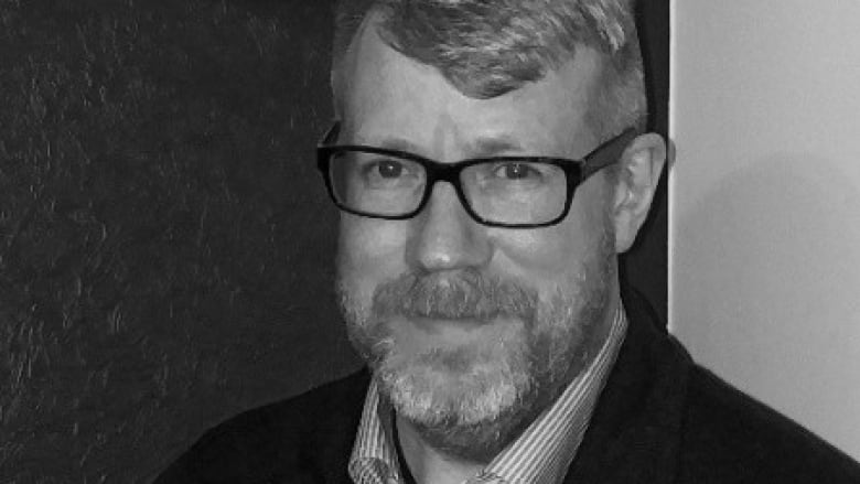 A black-and-white head-and-shoulders image of a bearded man wearing glasses.