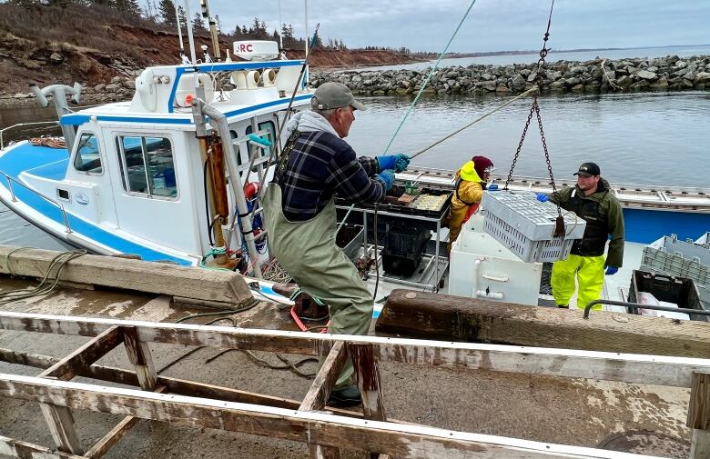 Two men on a fishing boat are seen while one on a deck hauls a lobster trap onto the boat.