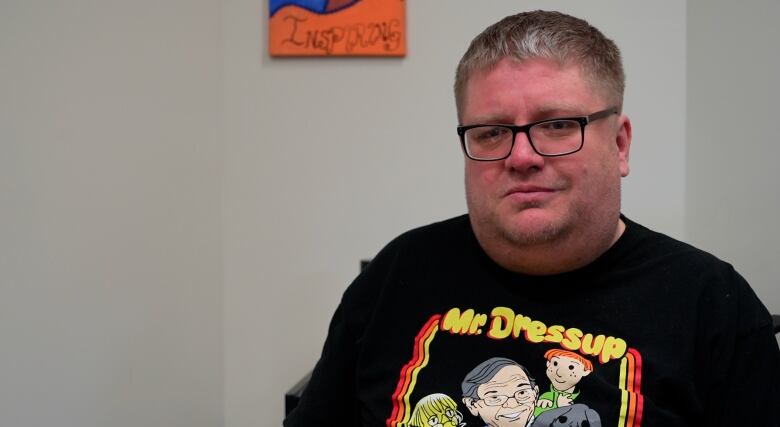 A man in a black mr. dressup shirt wearing glasses in front of a white background