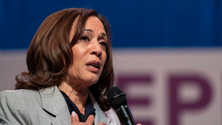 A woman wearing a blazer is shown in closeup holding a microphone.