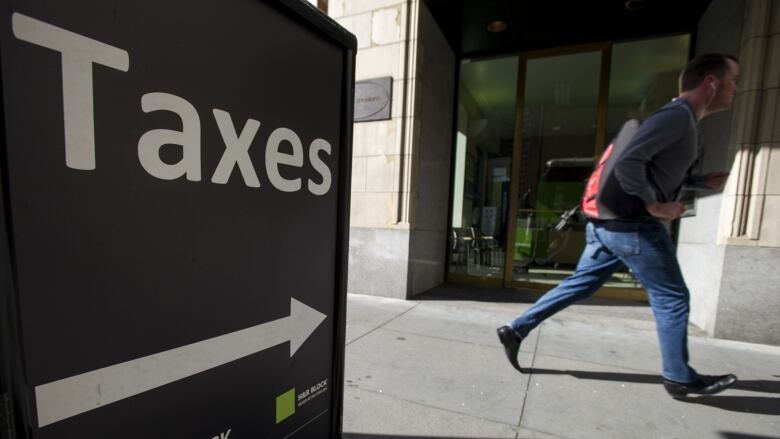 a man walks past a sign for an office of a well known tax preparation company.