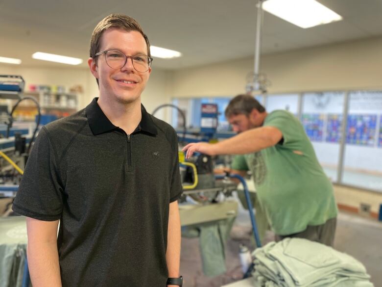 Chad Heron, Cows' CEO stands in the company's t-shirt production room, with workers' pressing shirts behind him. 