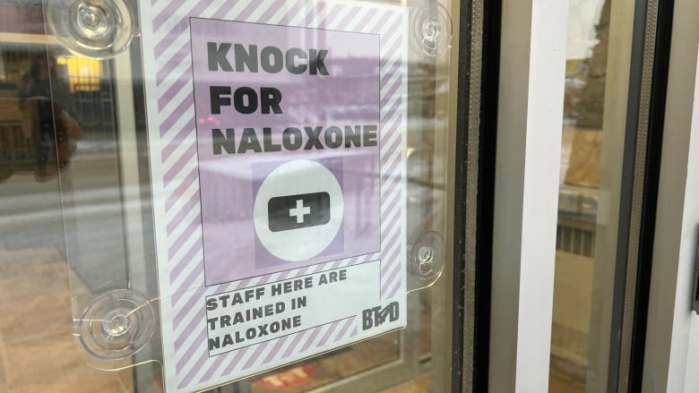 A sign on a glass door says, 'Knock for Naloxone.'