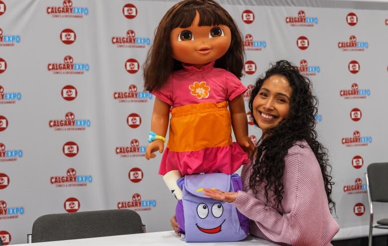 A woman stands with a Dora the Explorer doll.