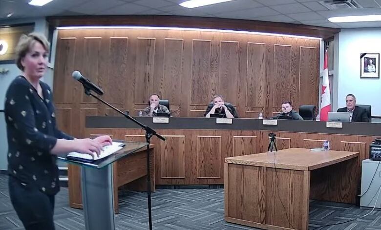 A woman speaks in front of a microphone before a row of city councillors.