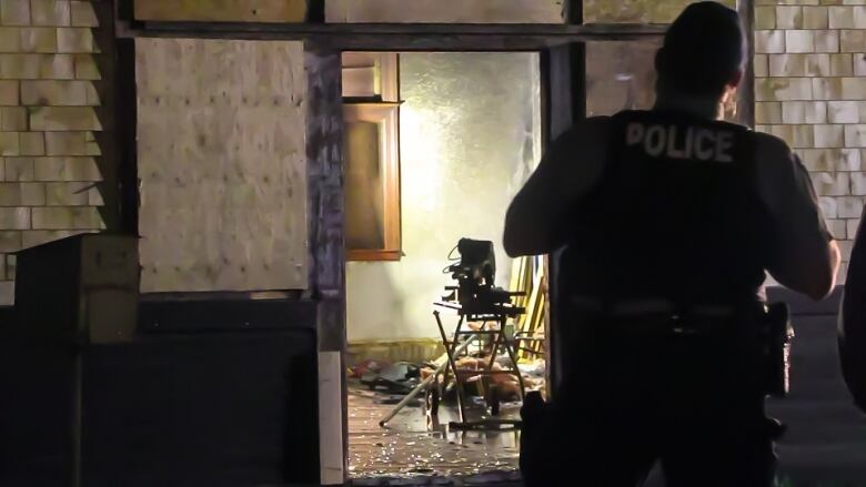 A police officer stands with his back turned and looks through a doorway at a room under construction. There's water on the floor.