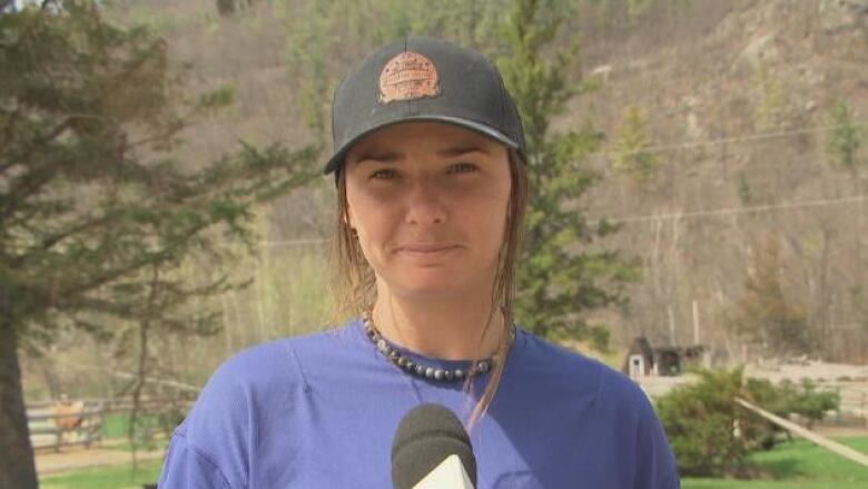 A woman in a ballcap and purple t-shirt is interviewed in front of a forested area.