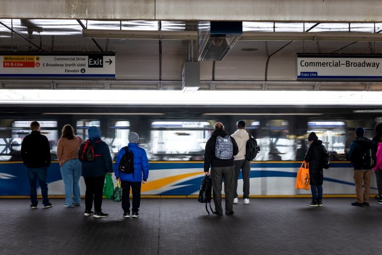 A number of people wait for a train at a public transit station.