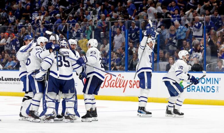 A group of male ice hockey players huddle together on the ice to celebrate a win.