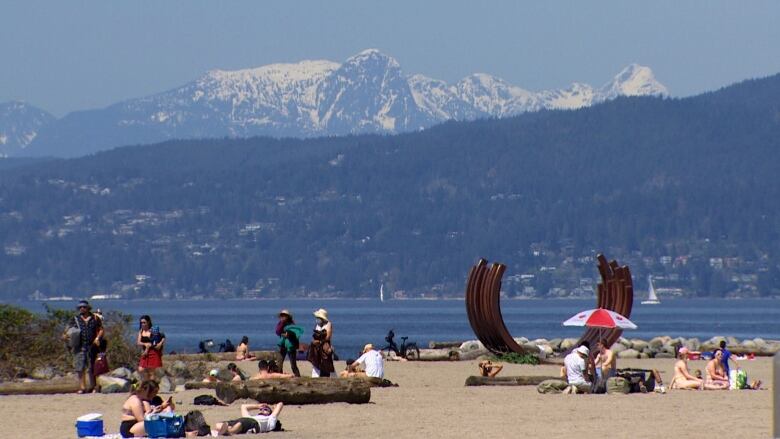 A view of people on a beach in Vancouver with snowcapped mountains in the distance.