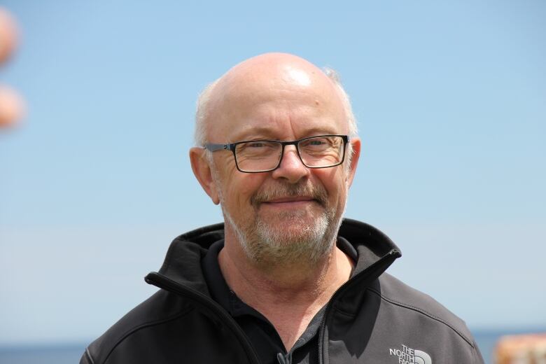 A man with glasses smiles and looks at the camera.