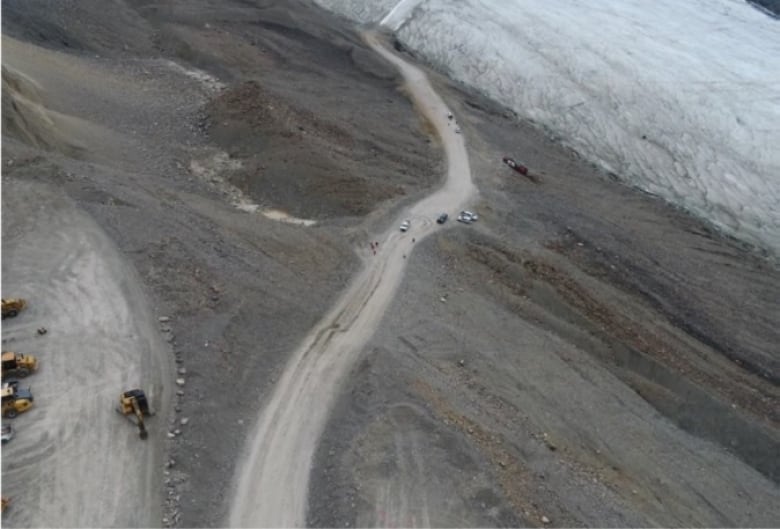 An aerial shot shows a bus lying beside a road, on a steep hill.