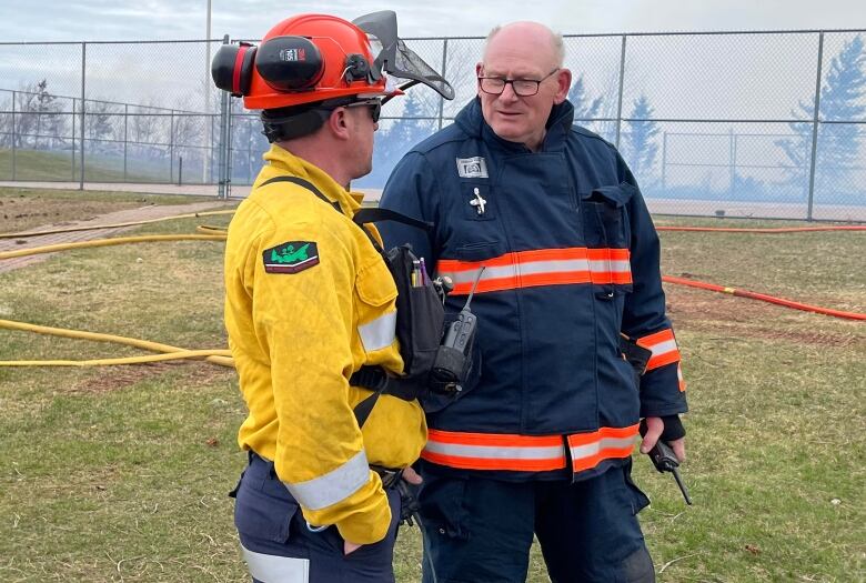 Man in fire uniform talks to man in yellow shirt with hard hat and breathing apparatus. 