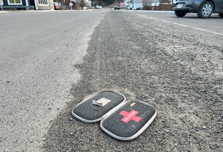 A used Naloxone kit is seen discarded on a city street.