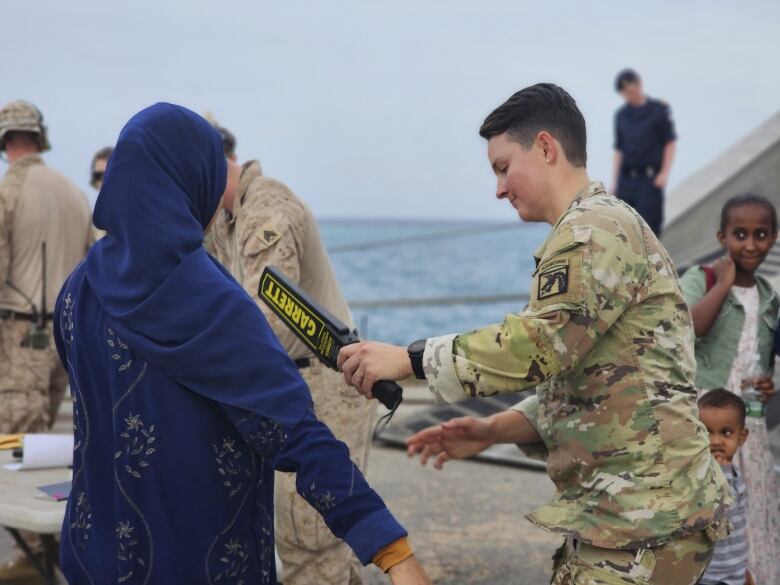 A U.S. soldier scans a woman with a metal detector before boarding a ship in Port Sudan.