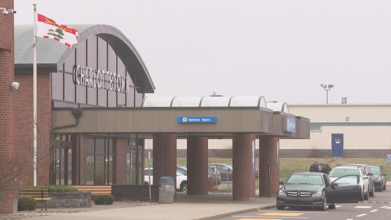 An exterior of the Charlottetown Airport terminal building. Cars are parked out front and a P.E.I. flag waves in the wind.