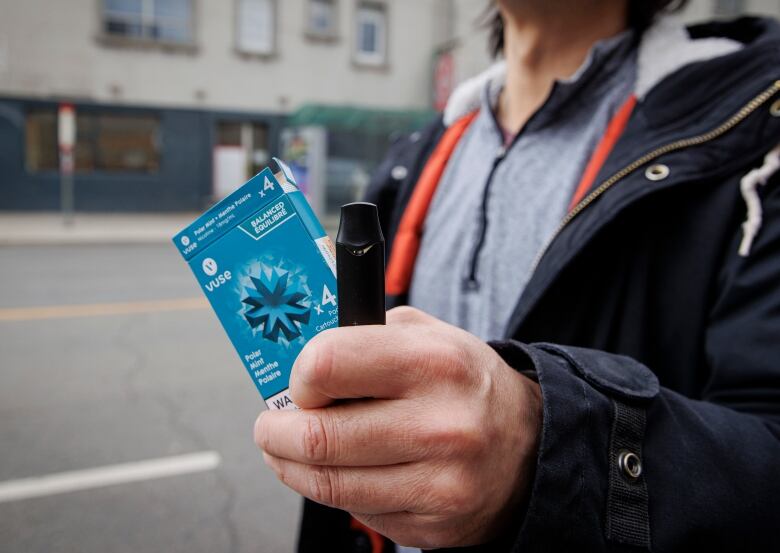 A man's hand is shown holding a vaping device and its blue packaging.