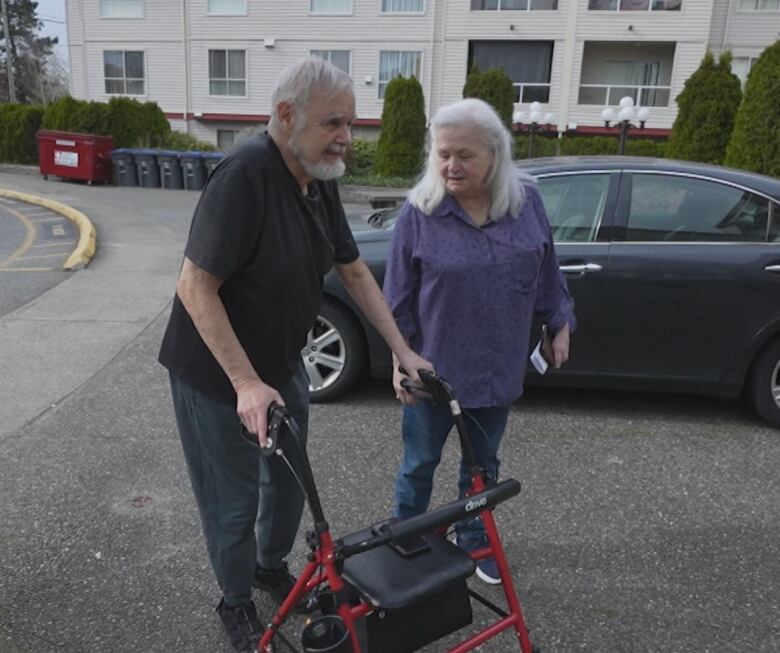 A man with a walker walks to an apartment entryway next to a woman.