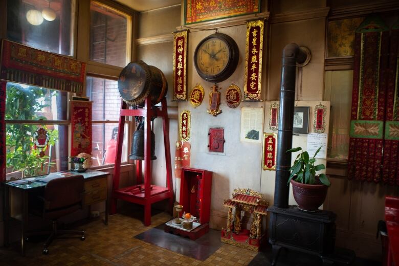 A room is pictured with an old stove, bell, and other decorative and spiritual objects. 