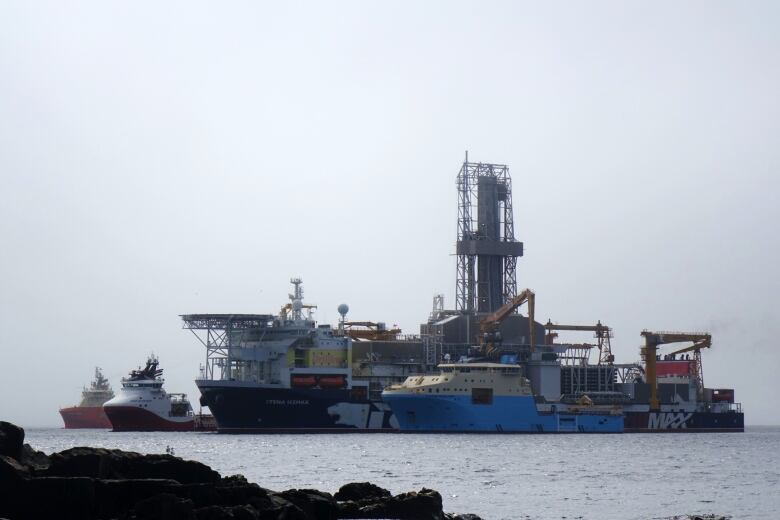 A large drilling ship sits in between three smaller vessels.