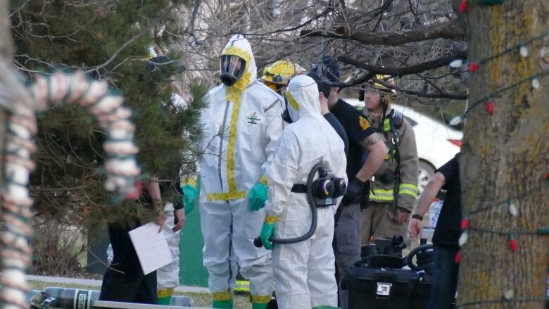 Firefighters and people in hazmat suits stand outside near trees covered with Christmas lights and other decorations.