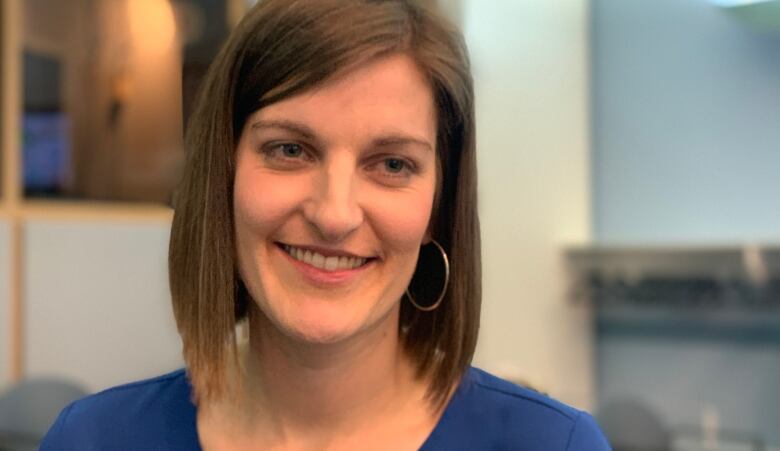 A woman in a blue shirt smiles while looking toward the camera.