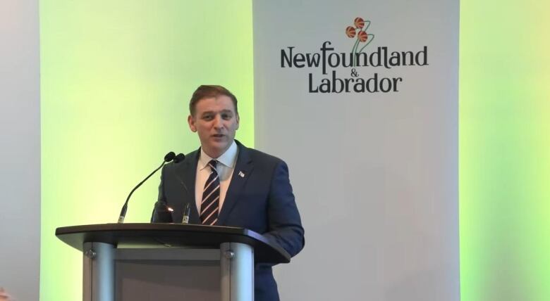 A man wearing a suit stands at a podium during a press conference.