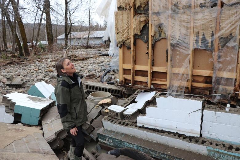 A woman stands looking at a damaged house