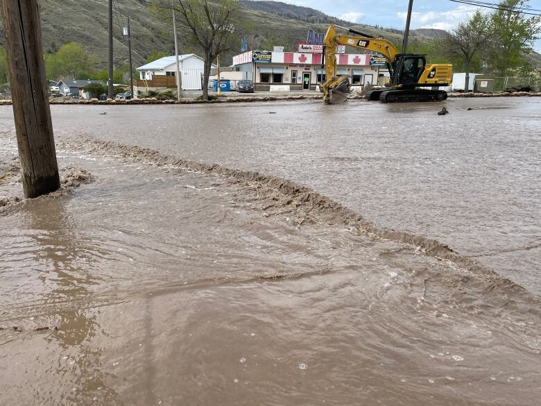 An industrial scoop attempts to place sandbags around a flooded area, with a strip mall visible in the background.