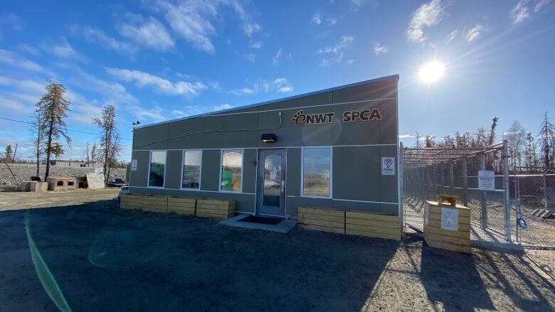 A building sits with flower boxes out front and four big windows. The sun shines in the background. 