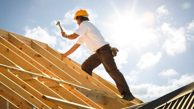 Roofer working on wooden roof structure of building on construction site.