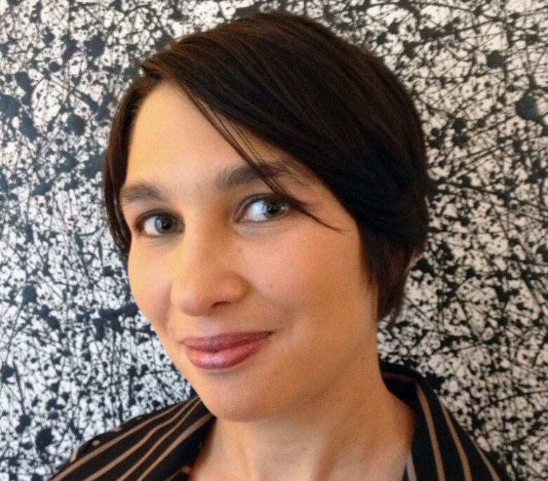 A woman wearing a brown striped shirt from the shoulders up. She is in front of a black and white abstract paint splatter background.