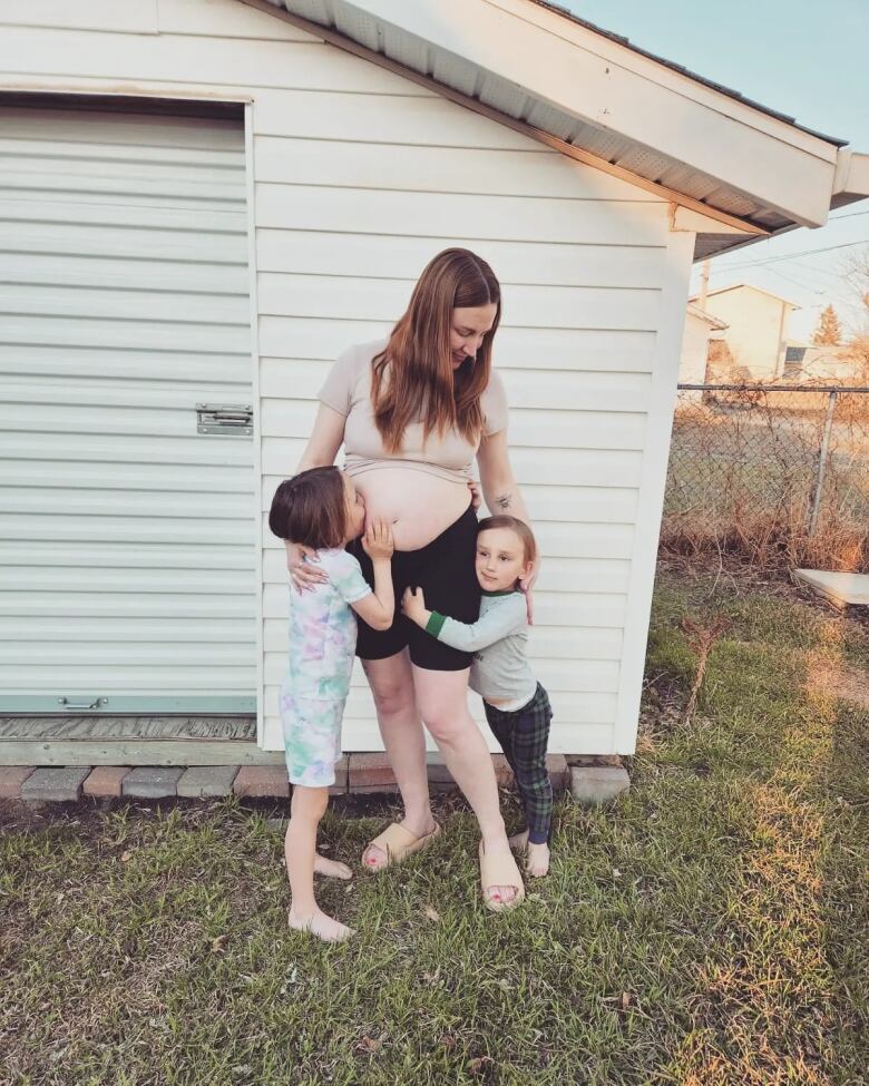 Two young children stand with a pregnant woman.