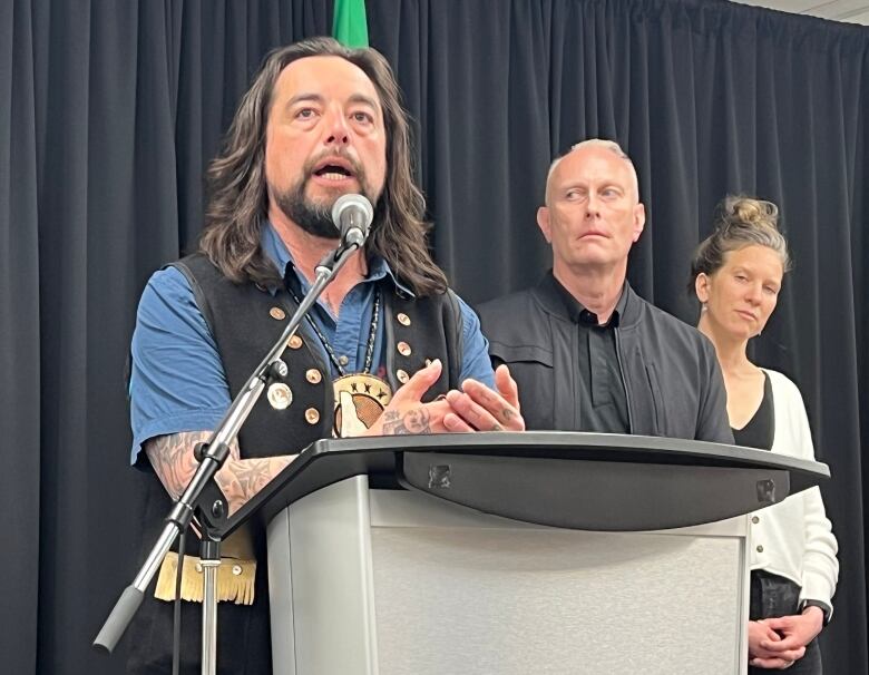 A man speaks from behind a podium while two people look on from behind.