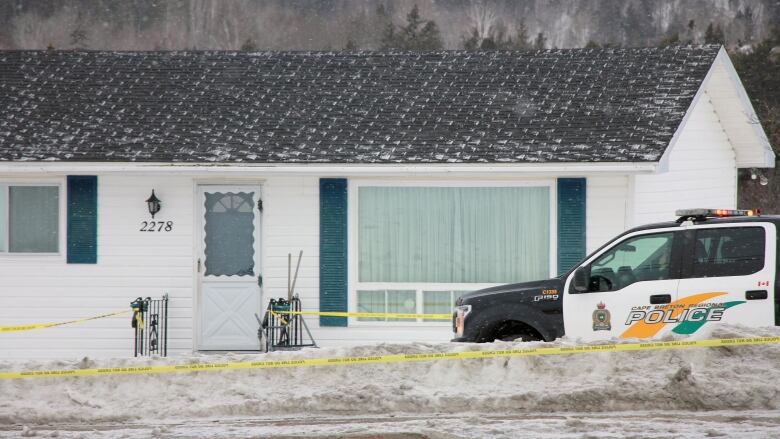 A black-and-white police car is parked in front of a one-storey home that has yellow police tape around the entrance.