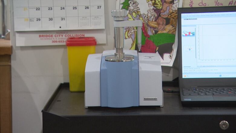 A grey and blue device that tests drug toxicity can be seen on a table along with a laptop. 