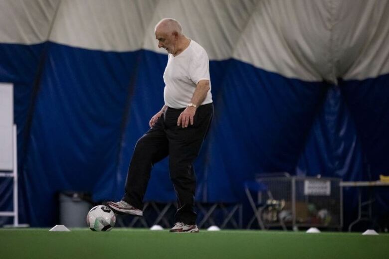 A man with a soccer ball at his feet navigates through a series of white cones on a green turf surface at an indoor facility.