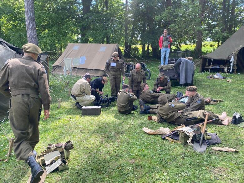 A group of men in second world war dress gather in the middle of a camp.