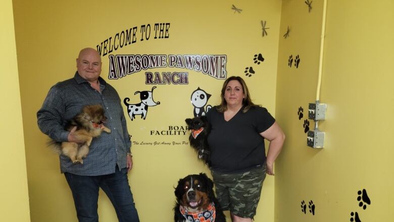 A man and woman and three dogs are standing in front of a yellow wall.