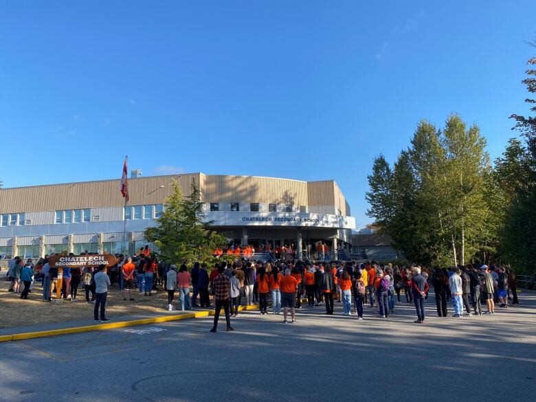 A group of students, some of whom are wearing orange, gather outside a school.