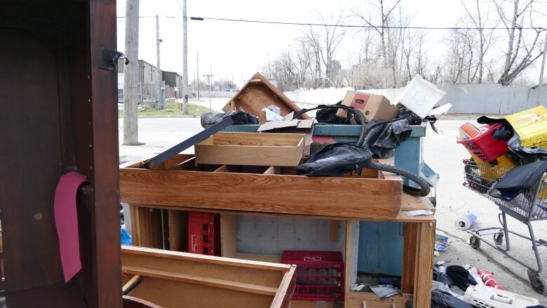 Wood furniture and a shopping cart full of garbage are left on the street outside a building.