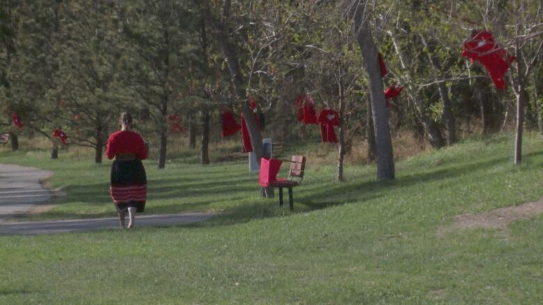 A woman wearing red walks past trees with red dresses hanging from them.