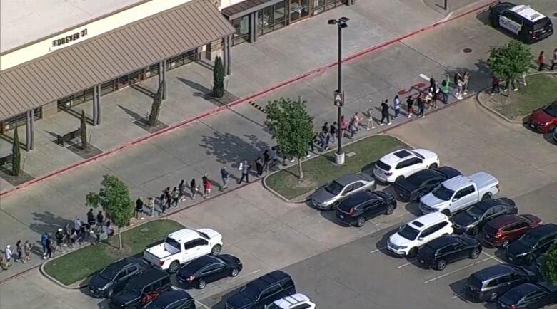 An aerial view shows a line of people with their hands up walking through a parking lot.