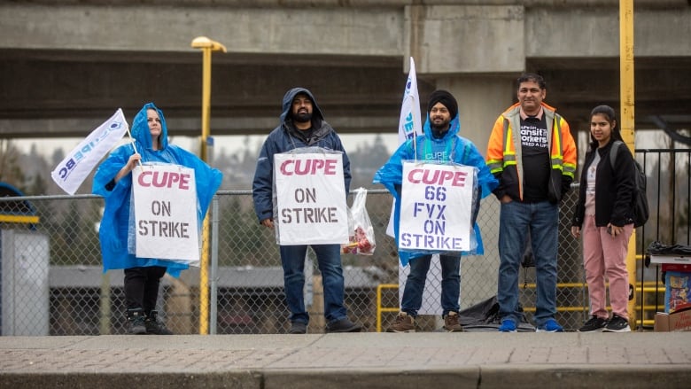 A number of striking workers hold up signs that read 'CUPE On Strike' amid rainy weather.