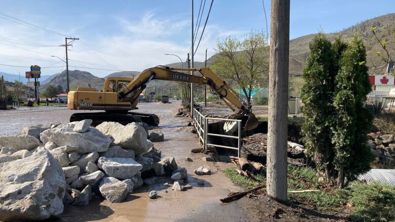 A front end digger scoops large boulders and rocks at a culvert on a street in Cache Creek B.C.